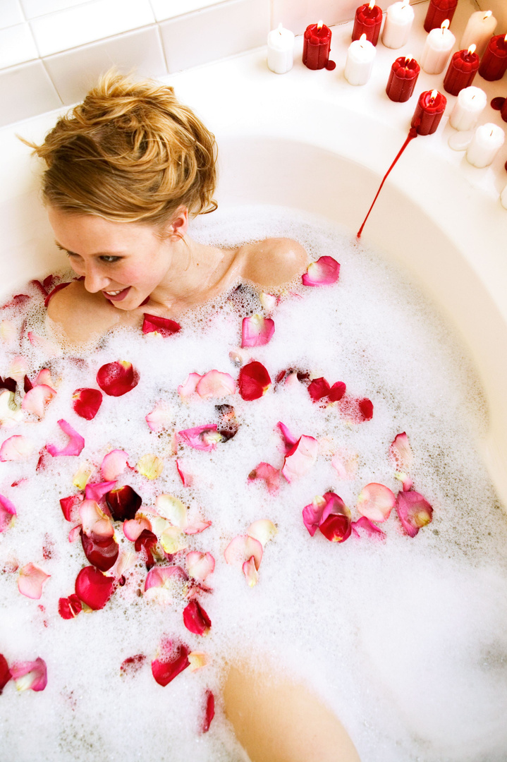 Woman soaking in bubble bath with rose petals